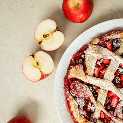Wide shot of large lattice pie with half cut apples on the side.